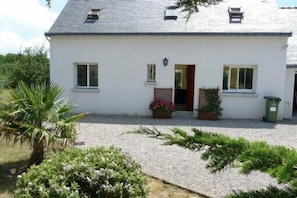 A white two-story house with a gravel driveway, a small garden with plants and flowers, and a door leading to the entrance. - Vacation home located in a cul-de-sac 800 metres from the beach (Erdeven)