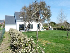 Una casa blanca con techo gris, un gran árbol en frente y un césped cuidado.