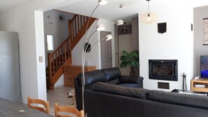 Un salon avec un canapé en cuir noir, une table à manger en bois avec des chaises, un escalier et une cheminée.