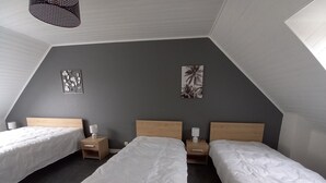 Une chambre avec trois lits, un plafond en pente et deux œuvres d’art accrochées au mur.