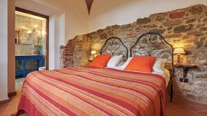 A bedroom with a stone wall, a bed with a striped blanket, two bedside lamps, and a nightstand. - Apartment with terrace and enchanting view (Torrita di Siena)
