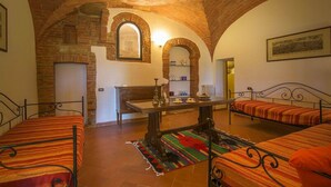 A cozy room with a brick ceiling, a fireplace, a dining table, and two beds with striped bedding. - Apartment with terrace and enchanting view (Torrita di Siena)