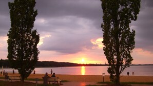 Vista del atardecer sobre un lago con un parque, bancos y árboles.