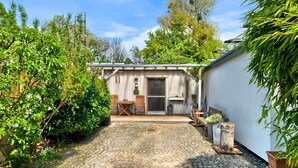 Un patio con una mesa y sillas de madera, un pequeño jardín y un edificio con puerta corredera.