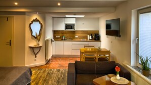 Un espacio habitable compacto con kitchenette, comedor y zona de estar con sofá y mesa de centro.