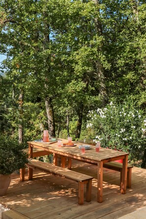 Eine Holzterrasse mit Tisch und Bänken, umgeben von Bäumen.
