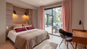 Une chambre moderne dotée d’un grand lit, d’un bureau et d’une chaise, et donnant sur une terrasse extérieure grâce à une porte-fenêtre coulissante.