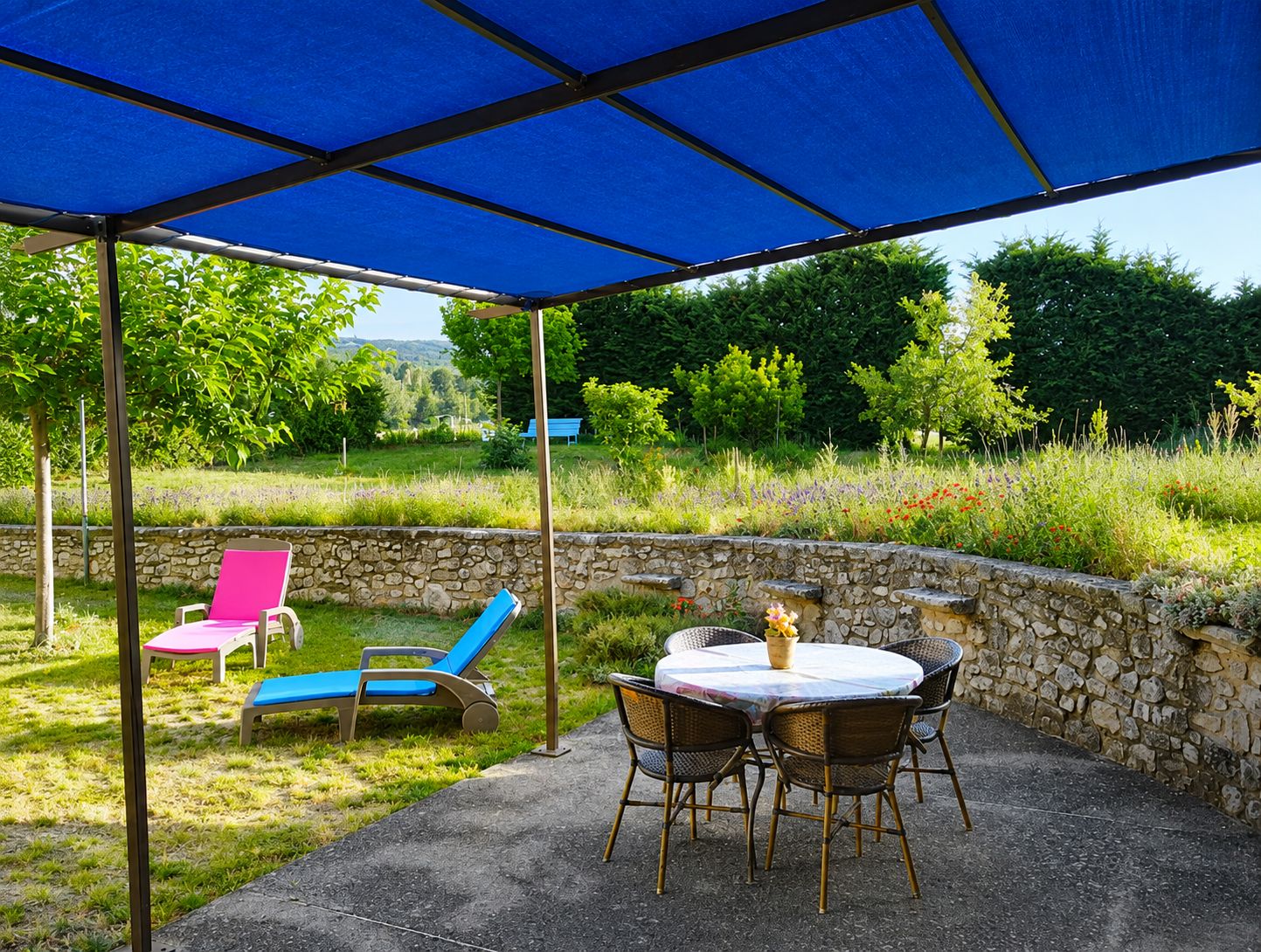 An outdoor patio with a table and chairs, a covered area with a blue canopy, and a stone wall.