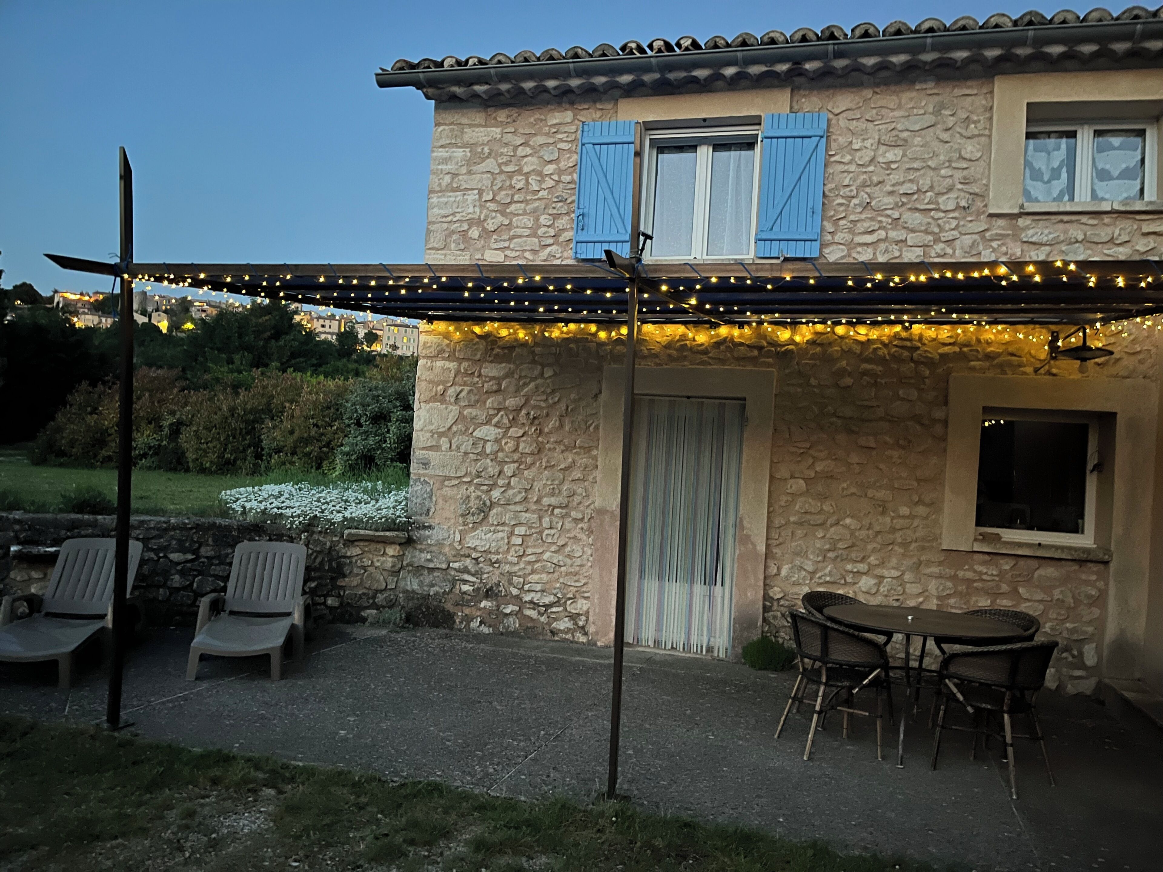 Een stenen huis met een overdekte patio, buitenmeubels en lichtjes.
