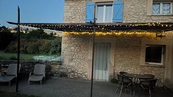 Een stenen huis met een overdekte patio, buitenmeubels en lichtjes.