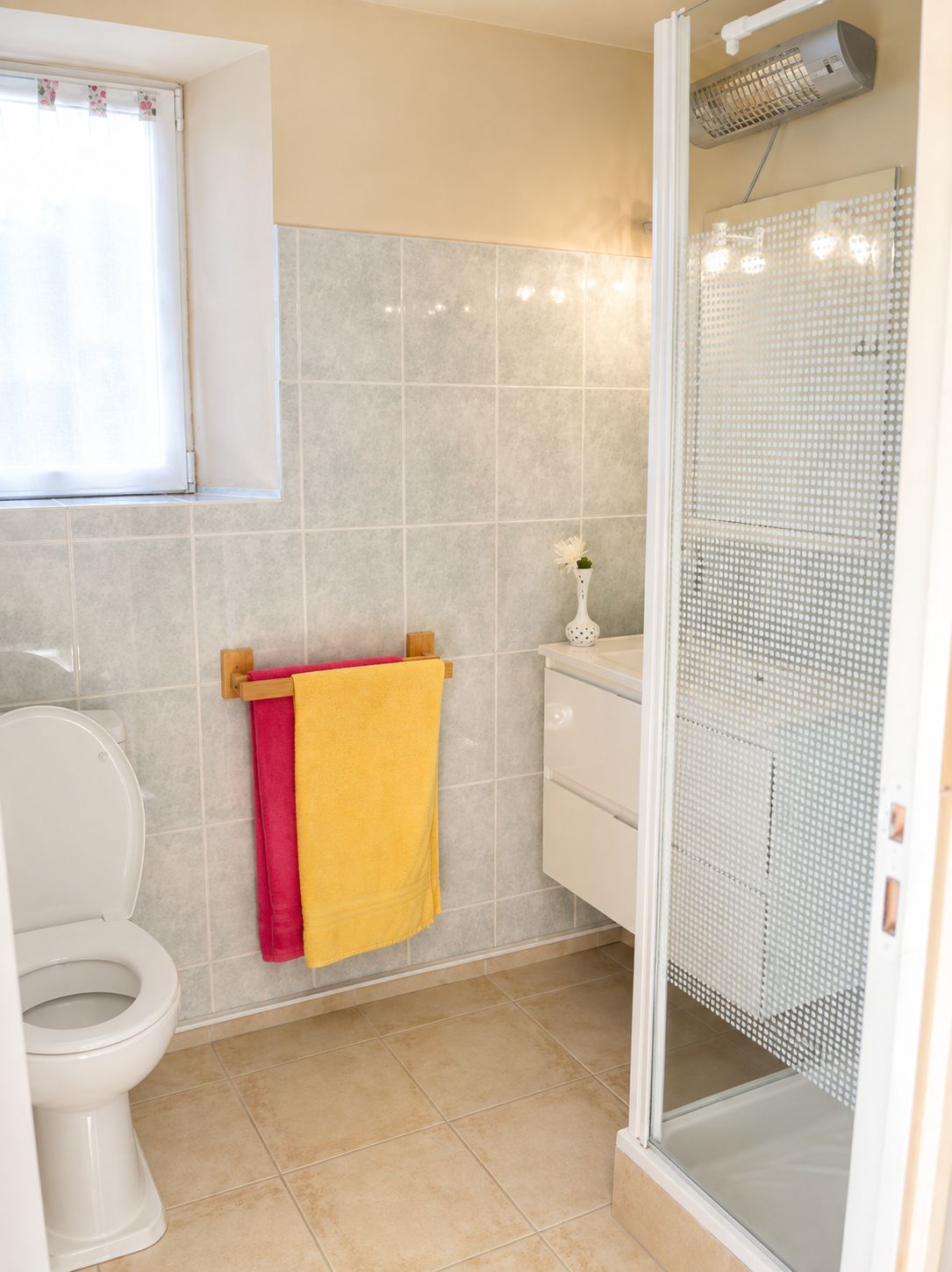 Un baño con inodoro, cabina de ducha y un perchero con una toalla amarilla.