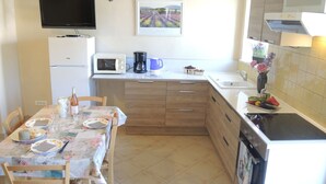 A small kitchen with a dining table, microwave, coffee maker, and a TV mounted on the wall. - Cottage rental at the foot of Mont Ventoux, surrounded by lavender cyclist (Sault)