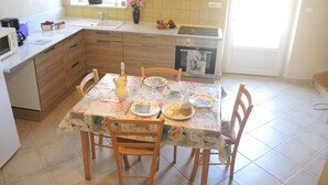 A kitchen with wooden cabinets, a dining table set with plates, and a microwave. - Cottage rental at the foot of Mont Ventoux, surrounded by lavender cyclist (Sault)