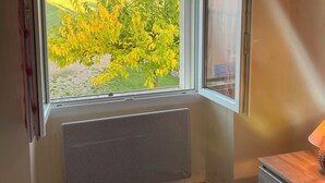 A bedroom with a large window, a radiator, a bed with a floral bedspread, and a wooden nightstand. - Cottage rental at the foot of Mont Ventoux, surrounded by lavender cyclist (Sault)