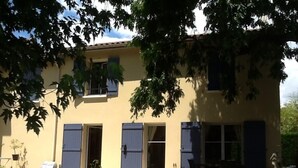 Een gebouw met twee verdiepingen, blauwe luiken, een klein voortuintje en potplanten.