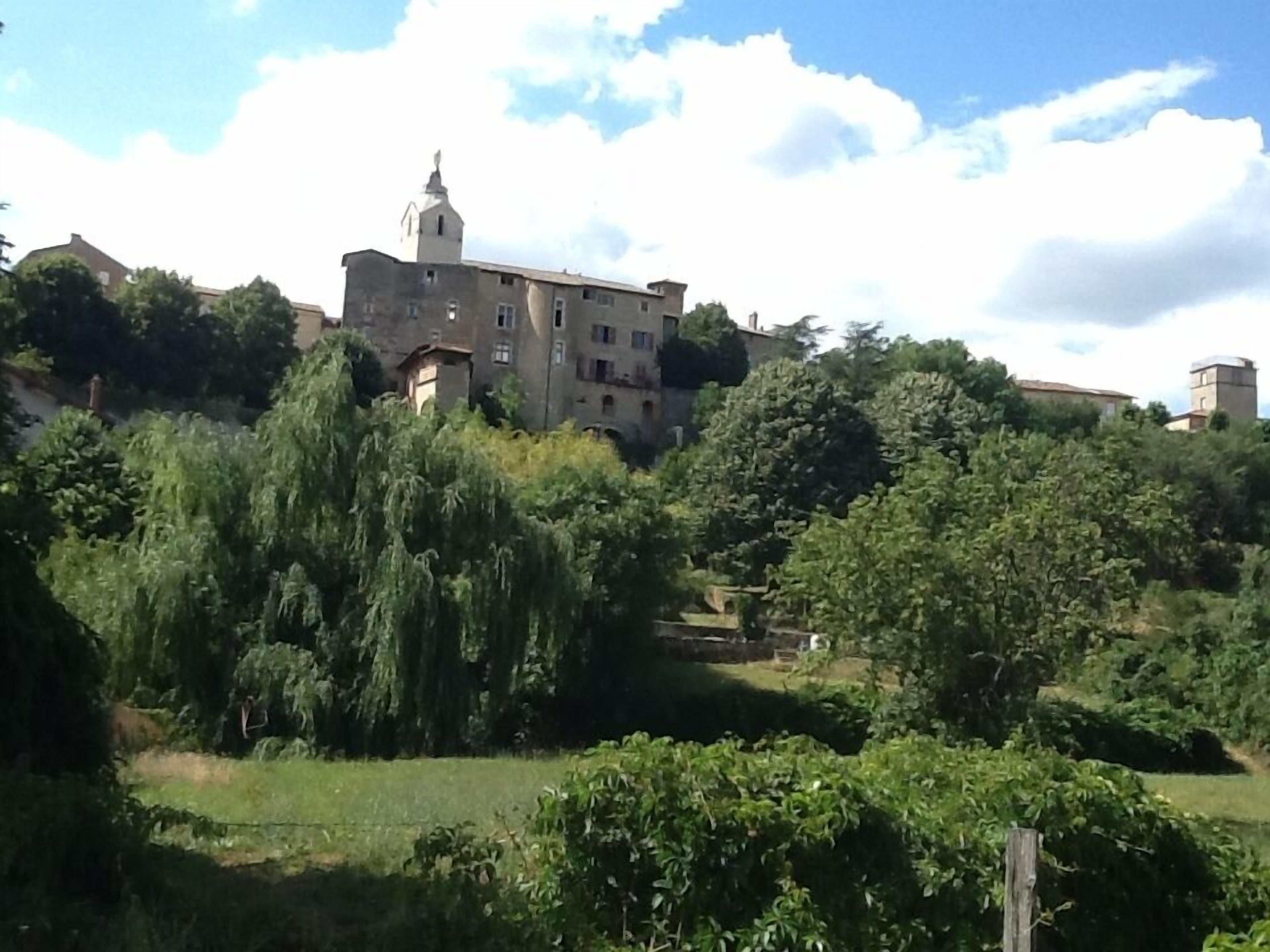 A large, historic building with a prominent tower, surrounded by lush greenery and other buildings in the background.