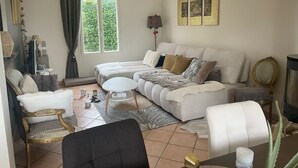 Een woonkamer met een bank, fauteuils, een salontafel en een televisie. Gordijnen, een lamp en kunst aan de muur.