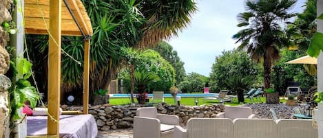 Un patio al aire libre con mobiliario de mimbre, piso de piedra y una piscina al fondo.