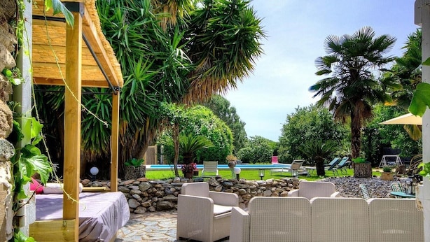 Ein Außenbereich mit Terrasse, Korbmöbeln, Steinboden und Pool im Hintergrund.