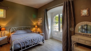 Ein Schlafzimmer mit einem Bett, Nachttischlampen, einem Fenster mit Vorhängen und einem Sessel.