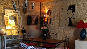 A cozy living room with a striped sofa, a dining table with chairs, a chandelier, and a stone wall with artwork. - Restored country house, in the spirit "Countryside" Charm " (Jau-Dignac-et-Loirac)