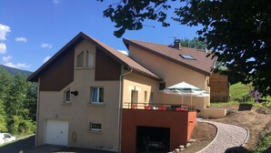 A two-story house with a sloped roof, a front garage, and a small outdoor seating area with an umbrella.