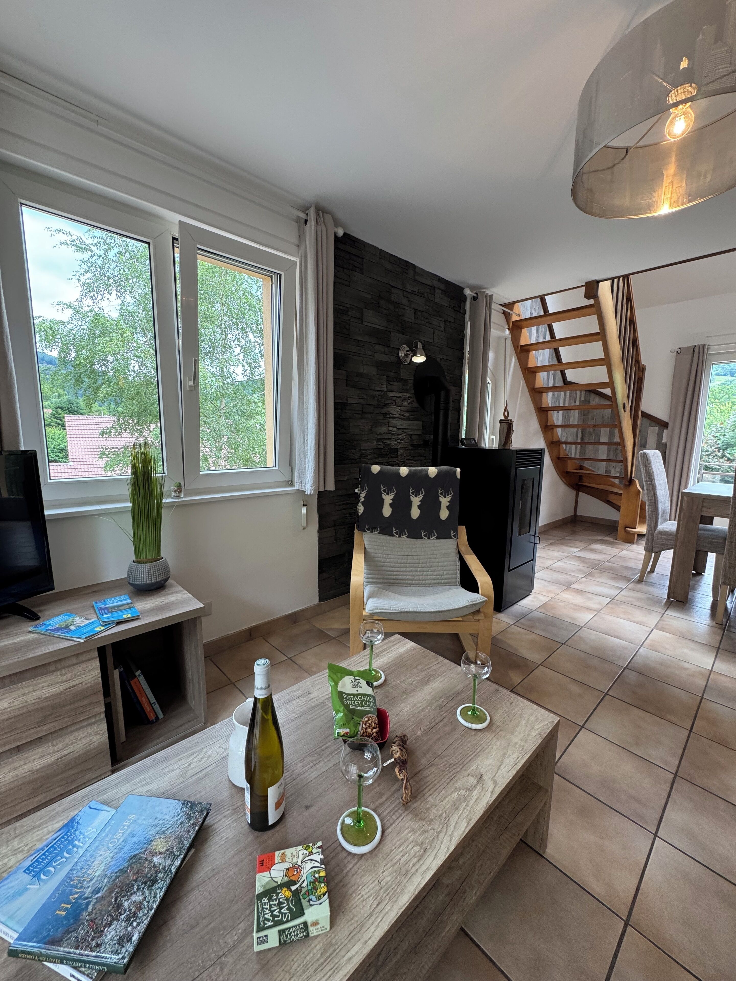 A modern living room with a wooden coffee table, books, a bottle of wine, and a chair.