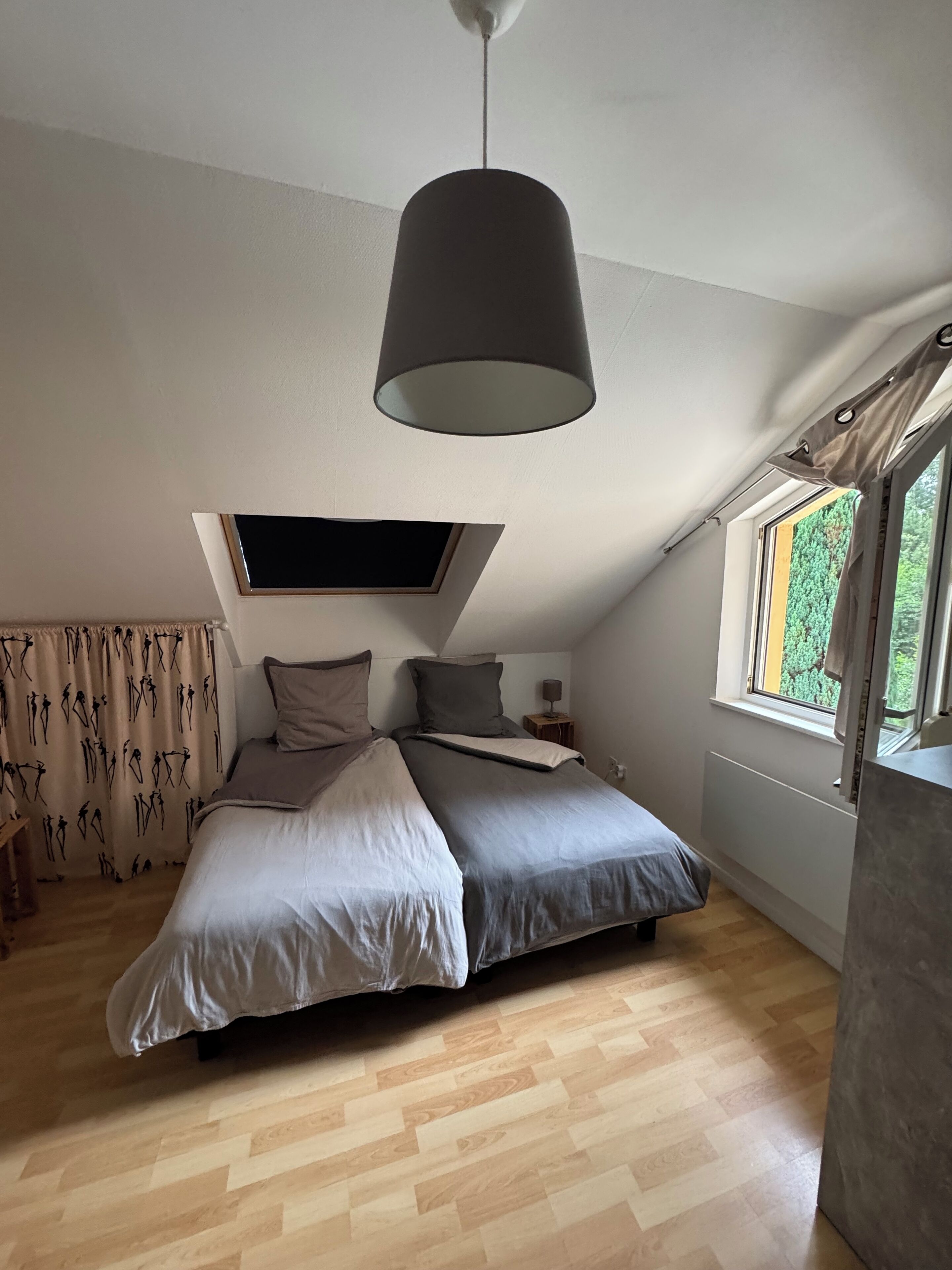 A bedroom with a bed, a ceiling fan, a window with curtains, and a view of greenery outside.