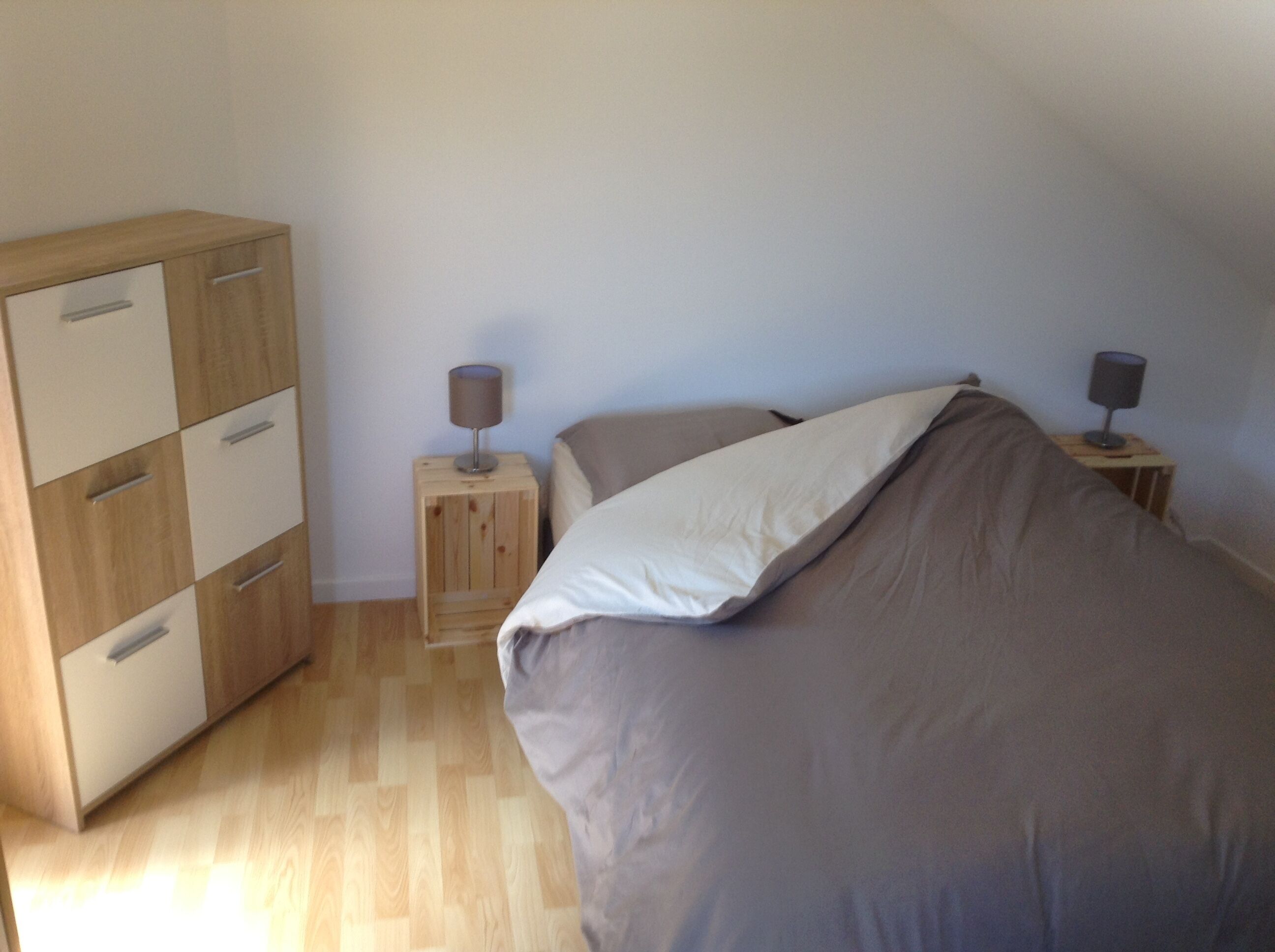 A bedroom with a bed, a wooden wardrobe, two bedside tables with lamps, and a light-colored wall.
