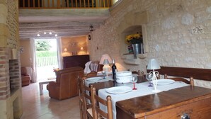 A dining area with a wooden table set for two, a stone wall, and a balcony with a wooden railing. - Charming house + private pool *** 8 pers - in CAPDROT in Perigord Pourpre (Monpazier Capdrot)