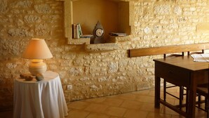 A stone wall with a built-in shelf holding books and a clock. A table with a lamp is in front of the wall. - Charming house + private pool *** 8 pers - in CAPDROT in Perigord Pourpre (Monpazier Capdrot)