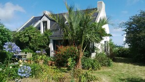 A house with a sloped roof, surrounded by lush greenery and flowering plants. - 4* villa with beautiful garden - 2 to 10 people (Bangor)