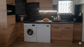 A compact kitchen with wooden cabinets, a washing machine, a bread loaf on the counter, and a window providing natural light. - Haven of peace Apartment 2 adults 2 children air-conditioned 60 m2 swimming pool (Porto-Vecchio)