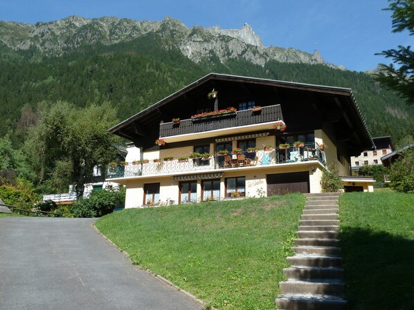 Ein zweistöckiges Gebäude mit Balkonen, einer Treppe, die zum Eingang führt, und einem Berg im Hintergrund.