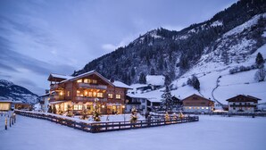 Un edificio grande de madera de varios pisos con balcones, rodeado de terrenos nevados y montañas.