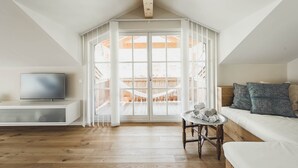 Un espacioso dormitorio tipo loft con un tragaluz grande, una zona de estar acogedora con un sofá y cojines, y un televisor de pantalla plana sobre un mueble blanco.