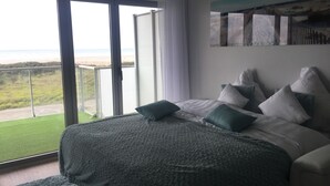 Een slaapkamer met een groot bed, uitzicht op het strand en een balkon.