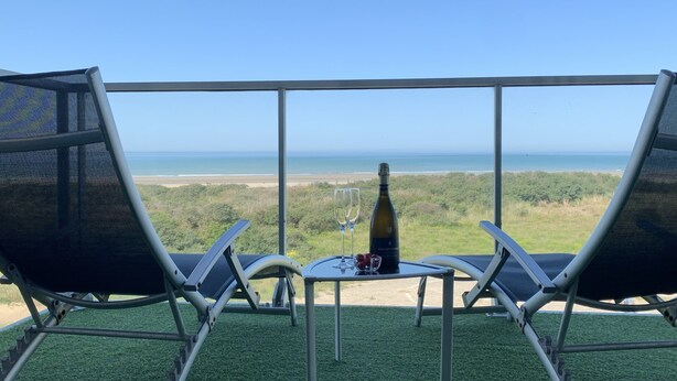 Een balkon met twee stoelen en een tafel, met uitzicht op een strand en de oceaan.
