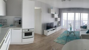 Een moderne woonkamer met een flatscreen televisie, een bank, een salontafel en een keukenhoek met een fornuis en een spoelbak.