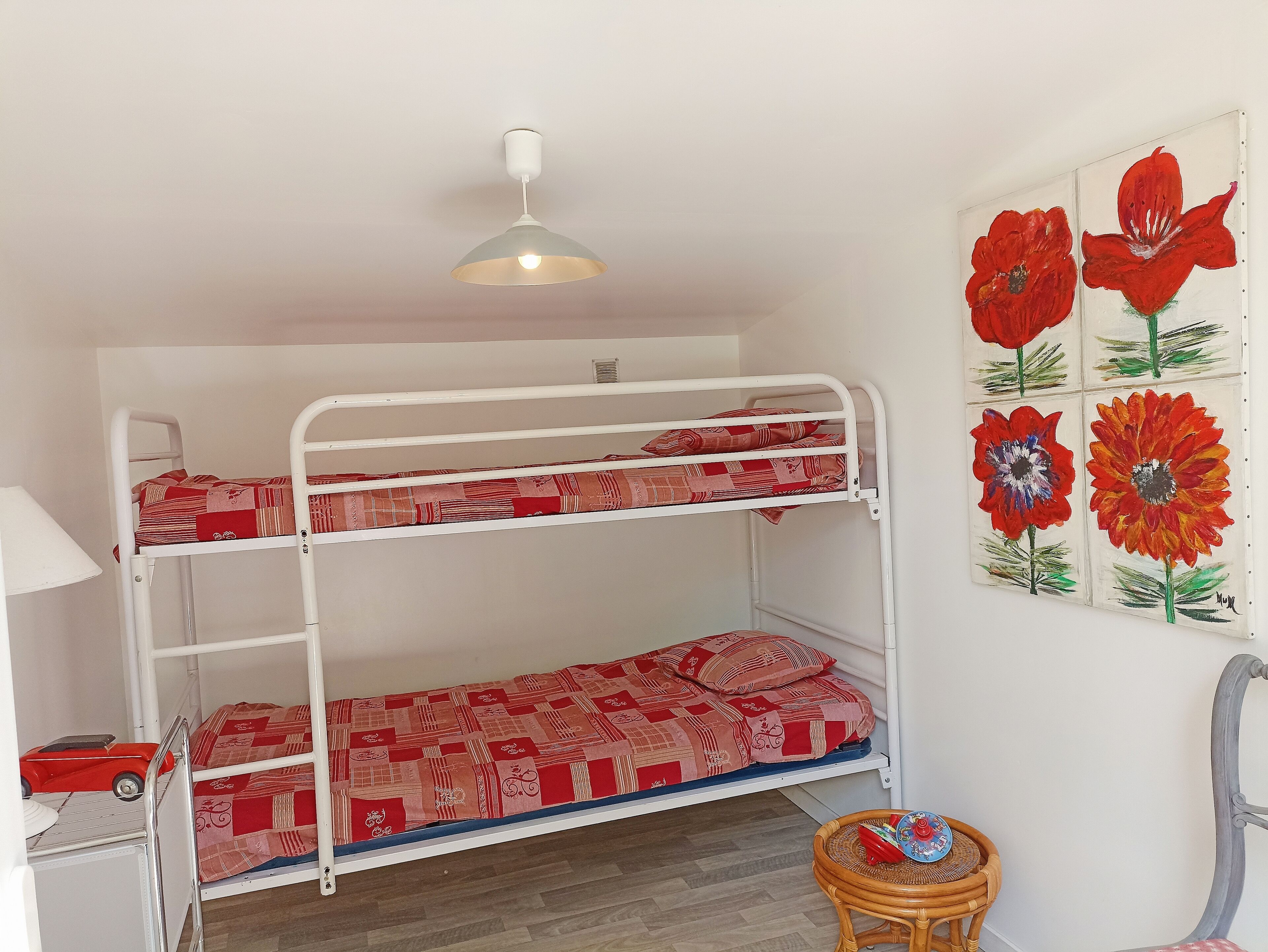 A bunk bed room with a ceiling light, a small table, and a wall with floral artwork.