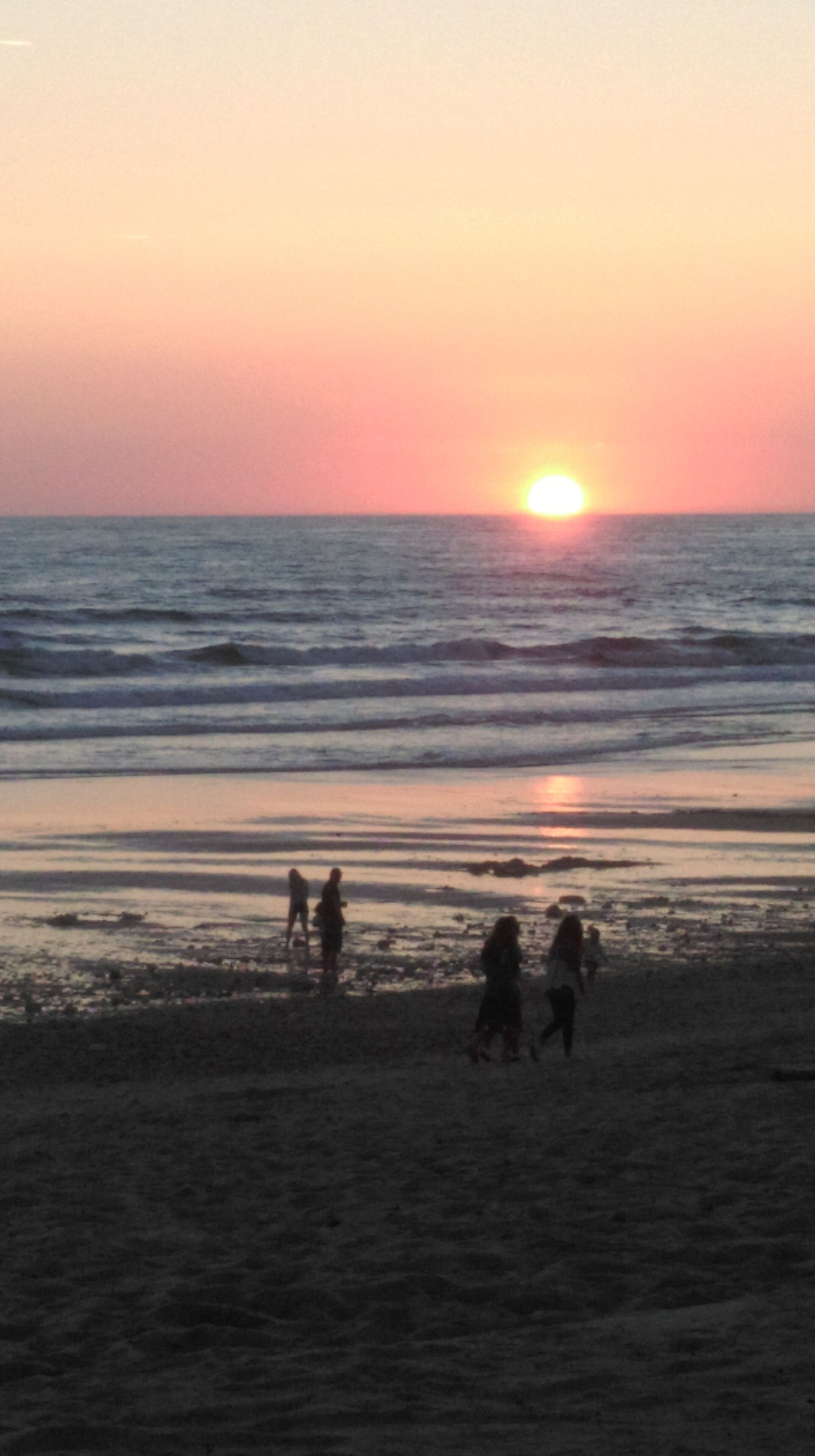 Un atardecer sobre el océano con gente caminando por la playa.