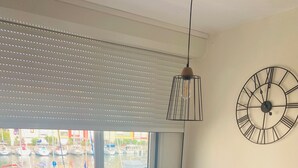 A dining area with a table, chairs, a hanging light fixture, and a wall clock. - STUDIO RENOVATED WITH VIEW ON BOATS FOR 4 PEOPLE (Agde)