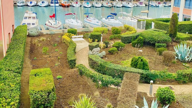 A marina with boats docked, surrounded by well-maintained gardens and buildings with balconies. - STUDIO RENOVATED WITH VIEW ON BOATS FOR 4 PEOPLE (Agde)