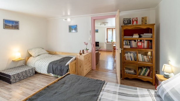 A cozy bedroom with a bed, bedside tables, a bookshelf, and a view into another room.