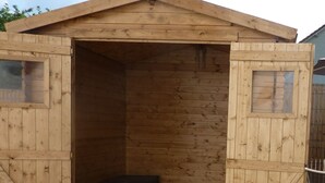 A wooden shed with a large open door, a bench inside, and a small window on the right wall.