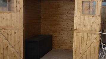 Un abri en bois avec une grande porte ouverte, un banc à l’intérieur et une petite fenêtre sur le mur de droite.