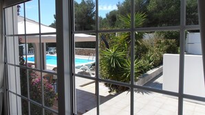 A view through a window of a pool area with a stone wall, lounge chairs, and potted plants.