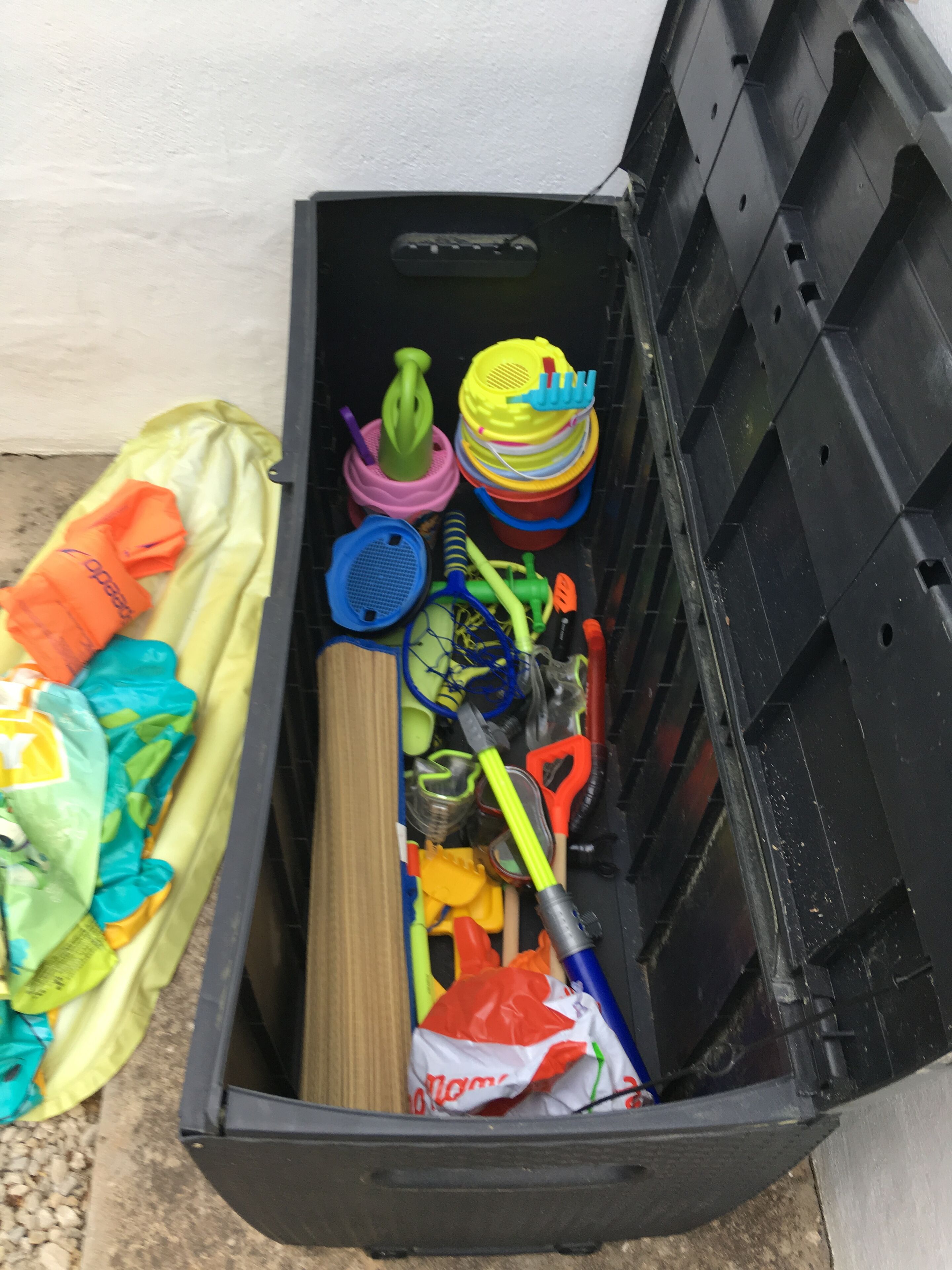 A black storage bin filled with various colorful items, including a yellow and green plastic container, a pink and yellow plastic item, and a red plastic bag.