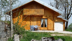 A wooden cabin with a balcony, a dining area with chairs, and a garage.