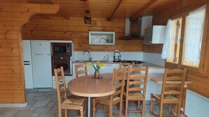 A wooden cabin interior with a kitchen, dining area, and a fireplace.